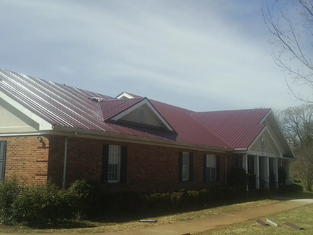 Red metal roof with gabled entries on a long brick building, from a Hail Damage Roof Repair job in Alcolu