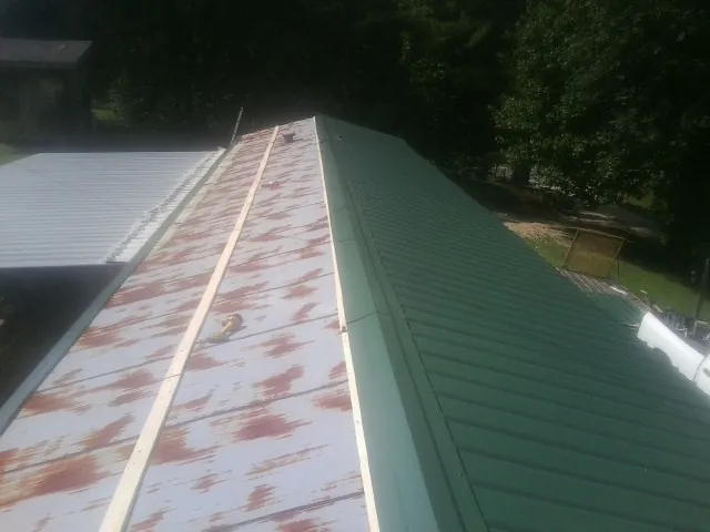 Old rusted panels beside newly installed green metal roofing — Wind Damage Roof Repair by Roofing Brothers in Alcolu