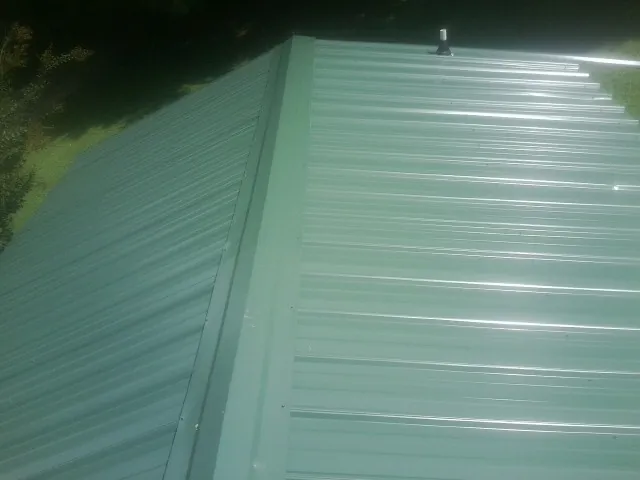New green metal panels meeting at the ridge of a roof — Flat Roof Repair work by our crew in Alcolu