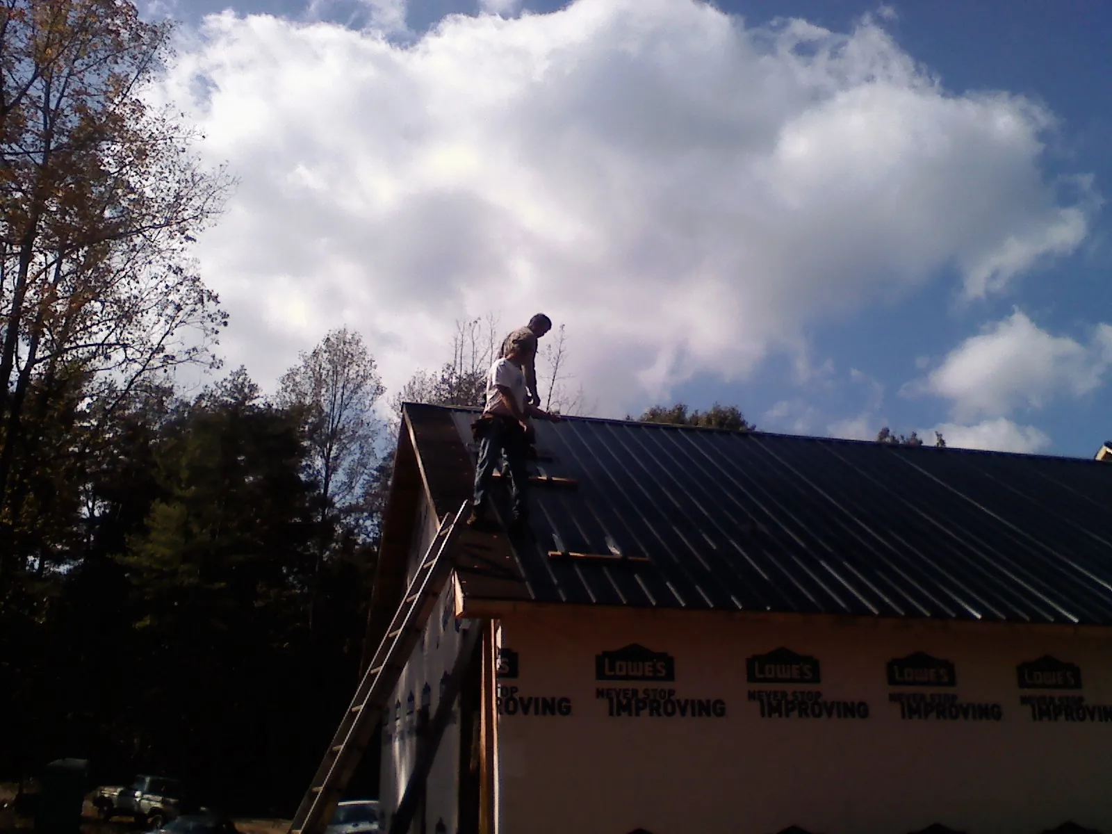 Roofer fastening dark metal panels high against a cloudy sky, from a Roof Inspection job in Alcolu