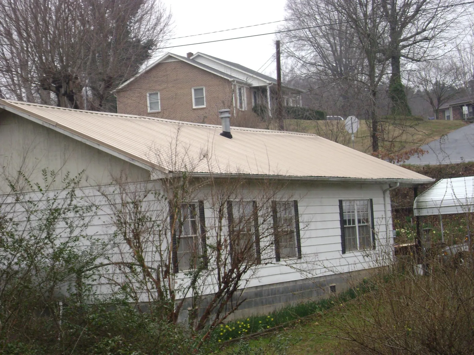 Tan metal roof on a white sided house set into a hillside — Commercial Roofing by Roofing Brothers in Alcolu